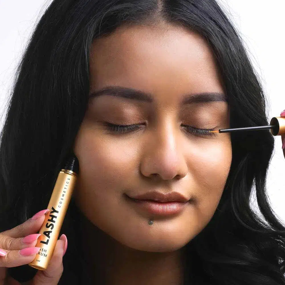 Front close-up of a Lashy Cosmetics model with eyes shut, applying Lashy Eyelash Serum to her left eyelashes.