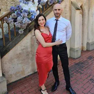 Couple posing together with the woman showcasing confidence and beauty in a red dress after having a positive experience with the eyelash growth serum featured in her testimonial.